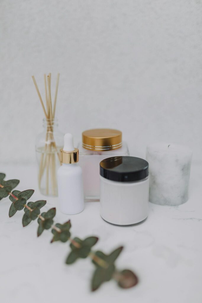 Minimalist display of skincare products, candle, and aromatherapy sticks on a marble surface.